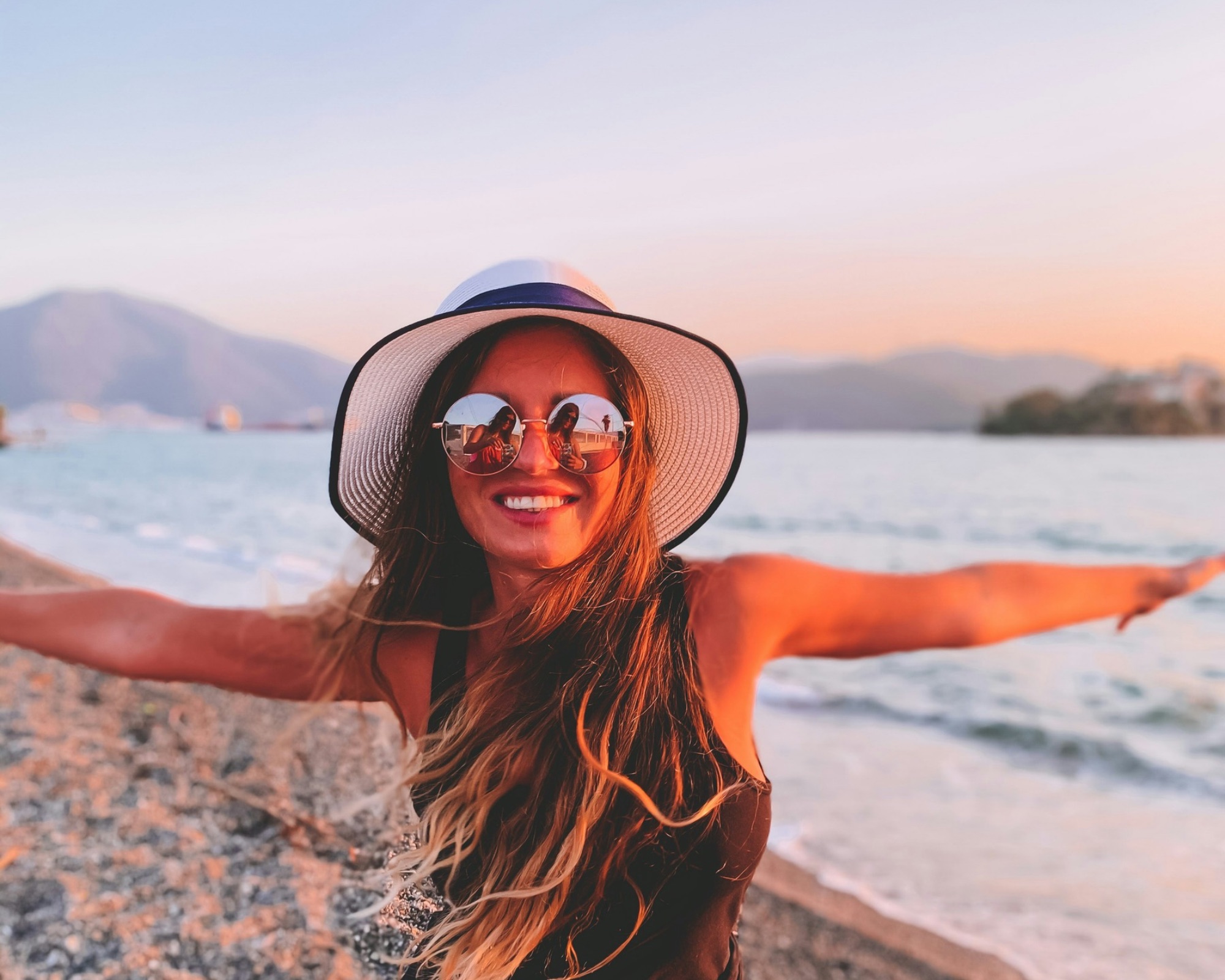 A traveller in a sun hat at the water's edge on a Greek beach at sunset
